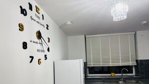Eine Küche mit Wanduhr, Kühlschrank, Fenster mit Jalousien und Spüle.