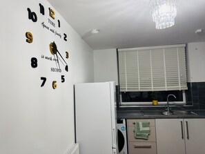 A kitchen with a wall clock, a refrigerator, a window with blinds, and a sink. - Modern 1BR Home in Clayton-le-Moors (Clayton Le Moors)