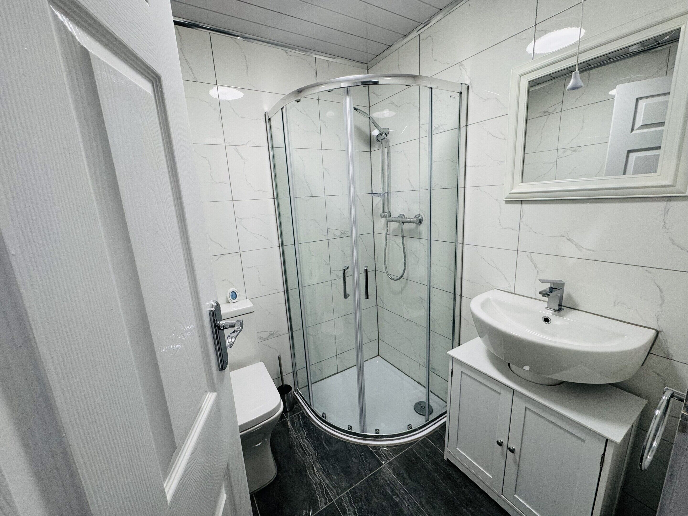 A modern bathroom with a glass-enclosed shower, a white sink, and a toilet.. Modern 1BR Home in Clayton-le-Moors