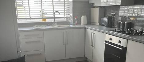 A modern kitchen with white cabinets, a built-in oven, and a window with blinds.