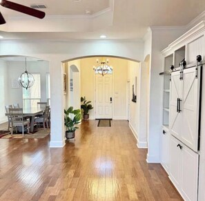 A spacious hallway with a wooden floor, a dining area with a table and chairs, and a kitchen with white cabinets.