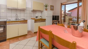 A compact kitchen with a dining area, including a table with chairs, a refrigerator, a sink, and a television. - Villa Estella Adriatic Residence (Vodice)