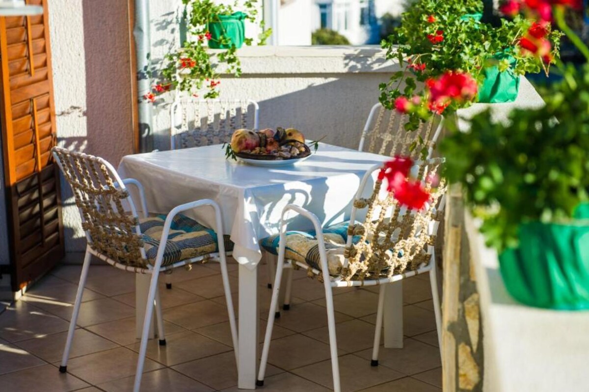 An outdoor patio with a table and chairs, a potted plant, and a window with a view.