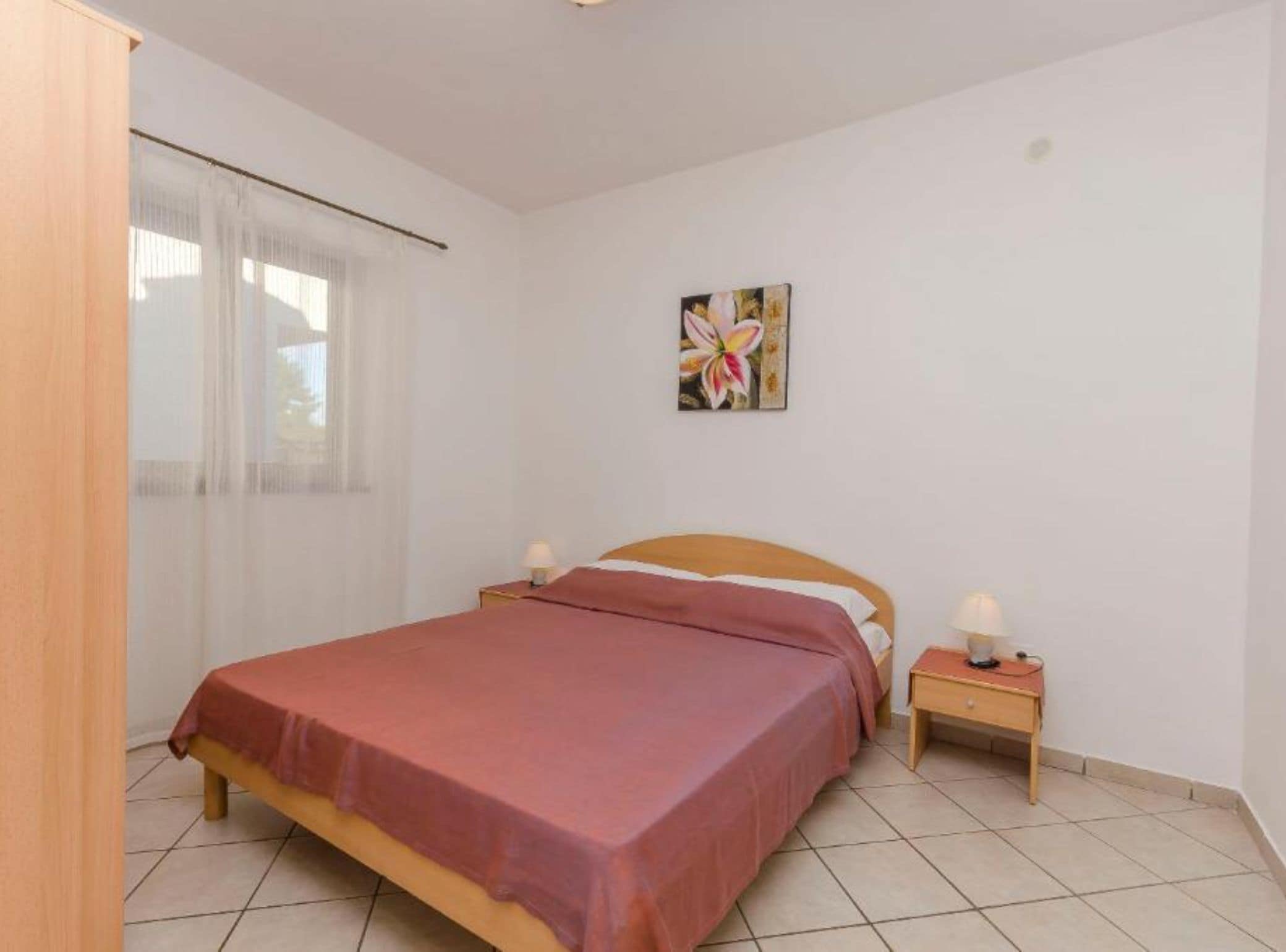 Ein Schlafzimmer mit einem Bett, zwei Nachttischen, einem Fenster mit Vorhängen und einem Wandbild.
