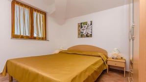 A single bed with a yellow bedspread, a nightstand with a lamp, a window with curtains, and a wall-mounted painting. - Villa Estella Adriatic Residence (Vodice)