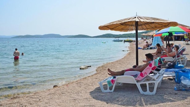 A beach with clear water, people swimming, and sun loungers under umbrellas. - Villa Estella Adriatic Residence (Vodice)