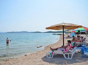 Uma praia com águas cristalinas, pessoas nadando e espreguiçadeiras sob guarda-sóis.