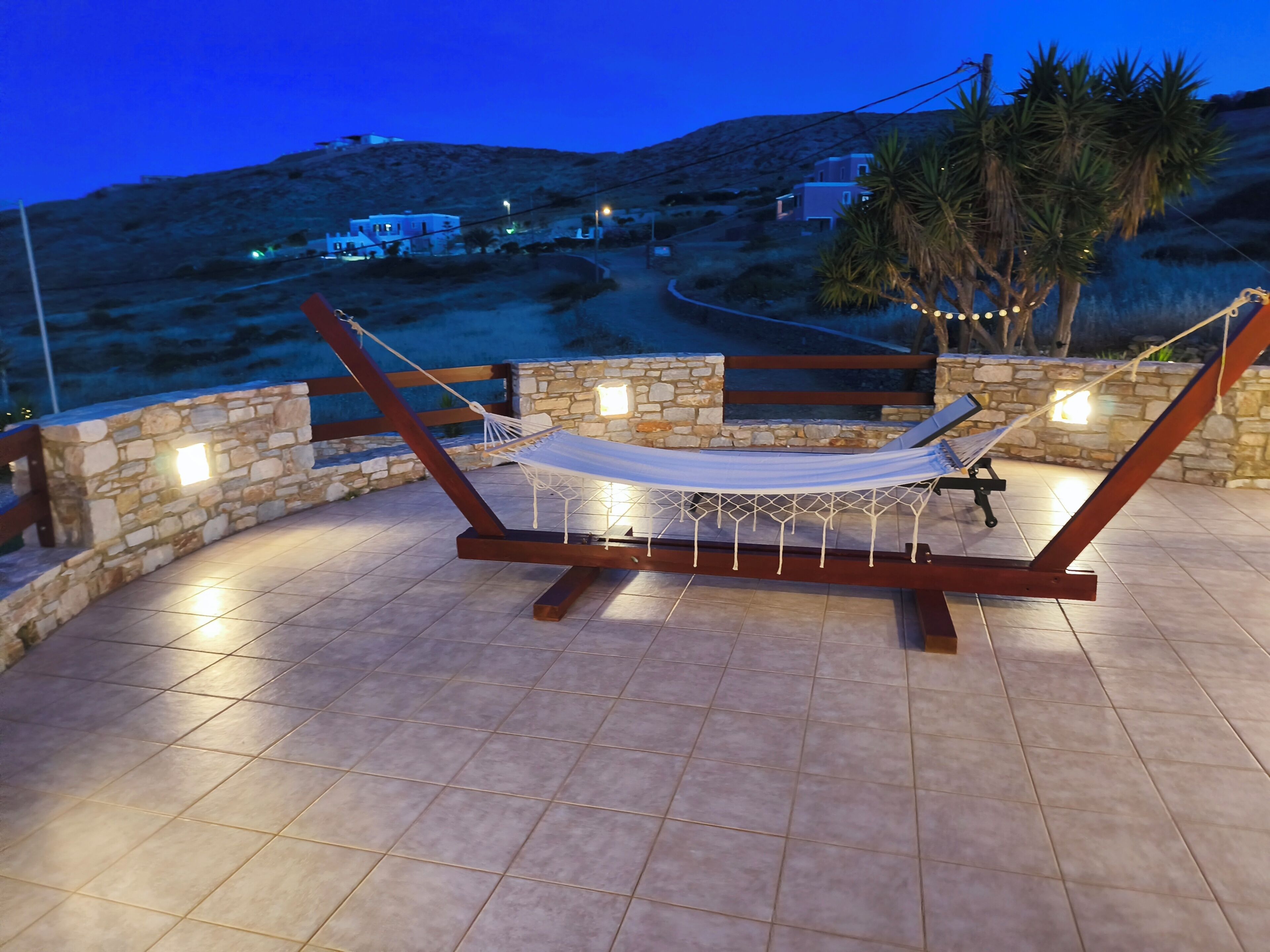 Una hamaca con mosquitera blanca, estructura de madera y paredes de piedra con luces.