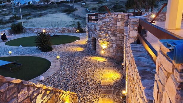 A stone staircase leading to a terrace with outdoor lighting, surrounded by a landscaped garden and a view of distant buildings. - PetraCasa: Luxury Sea View Villa with Premium Private Outdoor Spa (Azolimnos)