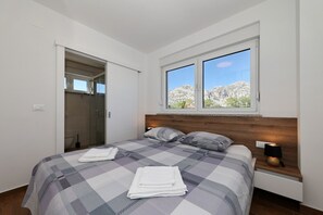 A bedroom with a bed, a nightstand, a window with a view, and a door leading to a bathroom. - Apartment Lux 1 near the Sea with Balcony (Starigrad)