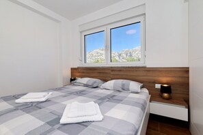 Ein modernes Schlafzimmer mit einem großen Bett, zwei Nachttischen, einem Fenster mit Blick auf Berge und einem hölzernen Kopfteil.