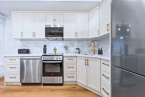 A modern kitchen with white cabinets, stainless steel appliances, and a marble countertop.