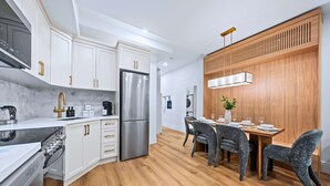 Eine moderne Küche mit weißen Schränken, Edelstahlgeräten und einem Essbereich mit Holzboden und grauen Sitzmöbeln.