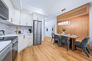 Une cuisine moderne avec des meubles blancs, des appareils en acier inoxydable et un coin repas en bois doté de chaises grises à revêtement.