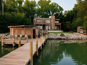 A modern wooden cabin with a dock extending into a lake, surrounded by trees.