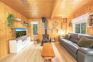 A wooden cabin interior with a sofa, a table, a TV, a fireplace, and shelves with plants. - Spa, Nature & Adventure | Chalet Le Vagabond (Saint-Léon-De-Standon)