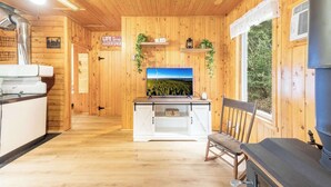 A cabin interior with wooden walls, a kitchen area, a dining table, and a large window.