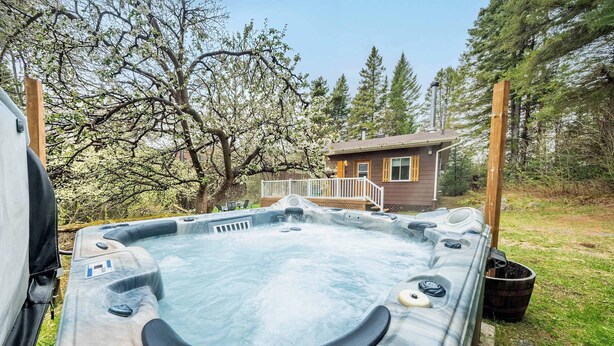 A hot tub with a wooden deck and a small cabin in the background.