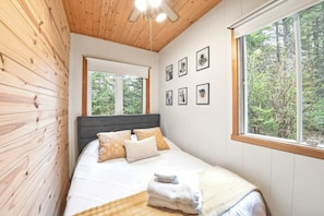 A bedroom with a wooden ceiling, a bed with white bedding, a grey headboard, and a window with a forest view. - Spa, Nature & Adventure | Chalet Le Vagabond (Saint-Léon-De-Standon)