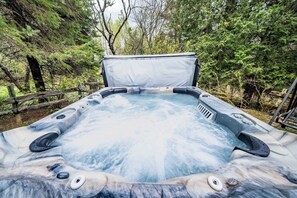 A hot tub in a forested area with a wooden deck and railings. - Spa, Nature & Adventure | Chalet Le Vagabond (Saint-Léon-De-Standon)