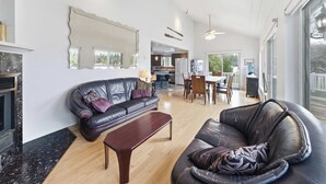 Uma sala de estar espaçosa com lareira, sofás de couro, área de refeições e um espelho grande.