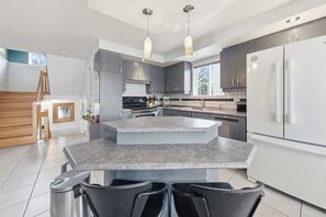 A modern kitchen with a central island, grey cabinets, stainless steel appliances, and pendant lighting. - Spa, Pool table & Lakefront | Maison aux Renards (Saint-Évariste-de-Forsyth)