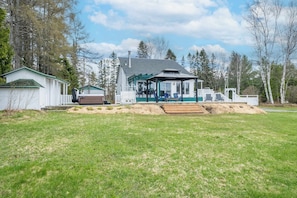 Ein zweistöckiges Haus mit überdachter Terrasse, Garage und kleiner Gartenhütte.
