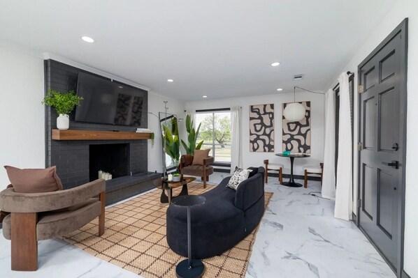 A modern living room with a black sectional sofa, a fireplace, a TV, and a large window.