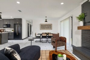 A modern kitchen with dark cabinets, a refrigerator, and a dining area with a table and chairs. - Home with Water Views Near
DFW, Arlington Stadiums (Irving)