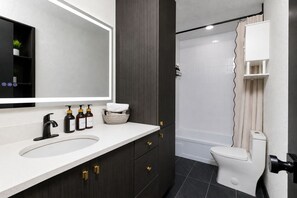 A modern bathroom with a large mirror, a sink with two bottles of lotion, a towel, and a shower area.