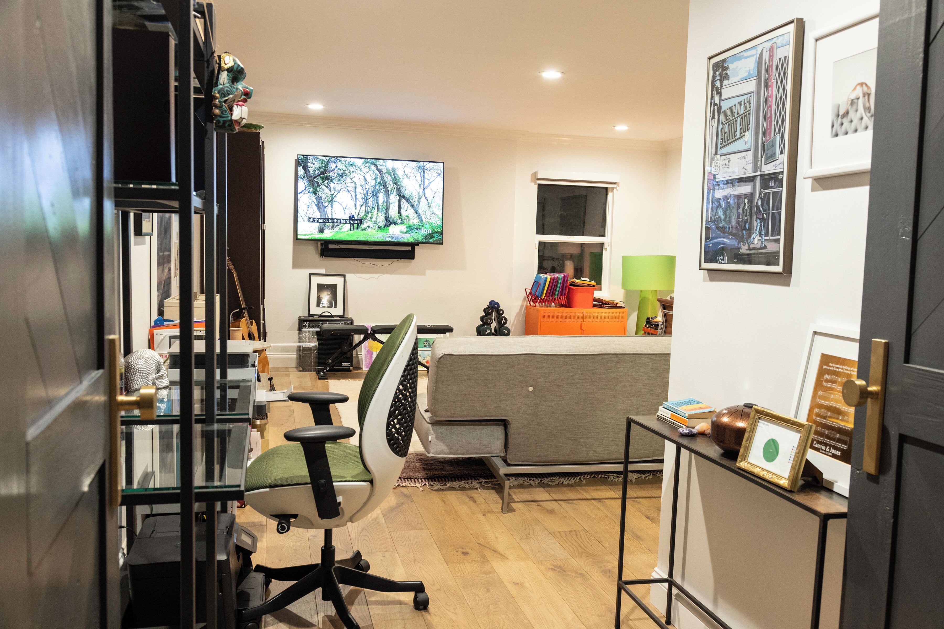 Un espacio de oficina moderno con un escritorio, una silla, un televisor y cuadros en la pared.