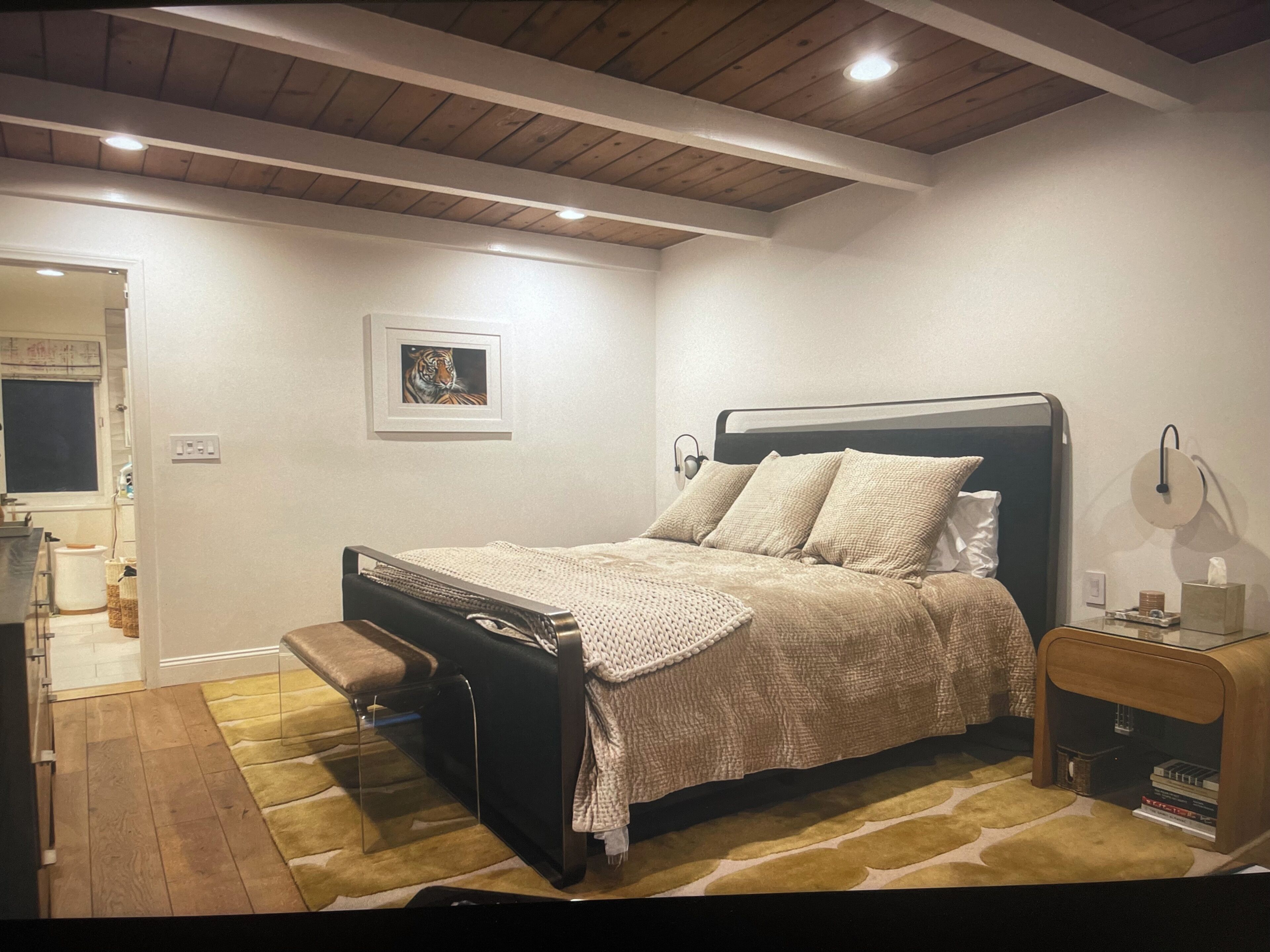 A bedroom with a bed, bedside tables, a bench, a wall-mounted light, and a framed picture.