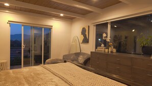Ein Schlafzimmer mit einem großen Bett, einem Schminktisch, einem Nachttisch, einer Lampe und Blick durch eine Schiebetür.