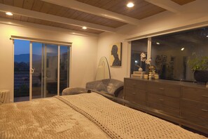 Ein Schlafzimmer mit einem großen Bett, einem Schminktisch, einem Nachttisch, einer Lampe und Blick durch eine Schiebetür.
