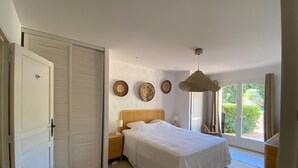 A bedroom with a bed, a nightstand, a lamp, and a view of the outdoors through a sliding door. - VILLA NEAR THE BEACHES OF PAMPELONE (Ramatuelle)