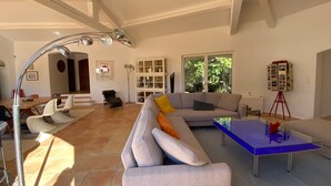 A spacious living room with a large sofa, a coffee table, and a dining area with chairs and a table. - VILLA NEAR THE BEACHES OF PAMPELONE (Ramatuelle)