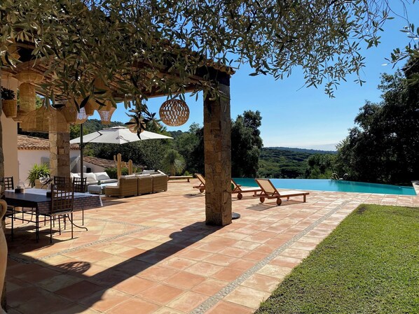 Eine Terrasse mit Pool, Gartenmöbeln und einer Pergola mit Sonnenschirmen.