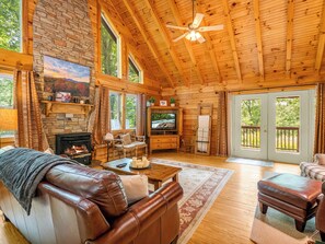 Ein gemütliches Blockhaus-Interieur mit Kamin, Ledersofa, Holzböden und einem Fernseher.