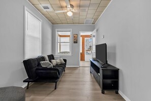 Ein modernes Wohnzimmer mit einer schwarzen Couch, einem Fernseher auf einem schwarzen Standfuß und einem Deckenventilator.