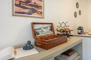 A wooden chest with a painting of a seascape, a bottle holder, and a notebook with a pen on a table. - Sand & Sail (Ostend)
