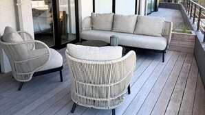 A balcony with a sofa and wicker chairs, a sliding glass door, and a view of buildings.