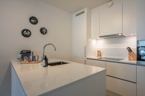 Et moderne køkken med hvid bordplade, stålvask og indbygget ovn.