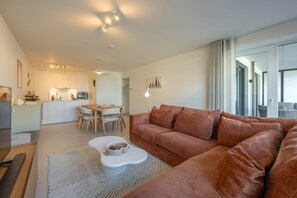 A modern living room with a sofa, a coffee table, and a dining area with chairs. - Sand & Sail (Ostend)