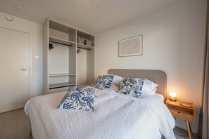 Een slaapkamer met een bed, nachtkastje, bedlamp, kledingkast en een lijst aan de muur.