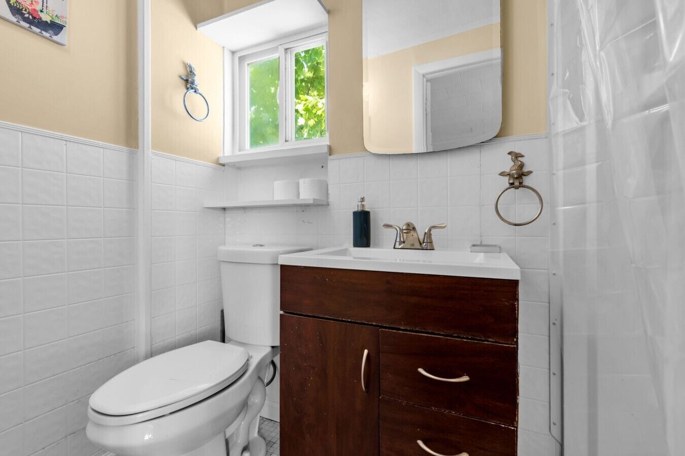 A bathroom with a toilet, a sink with a mirror above it, and a window with a view of greenery.