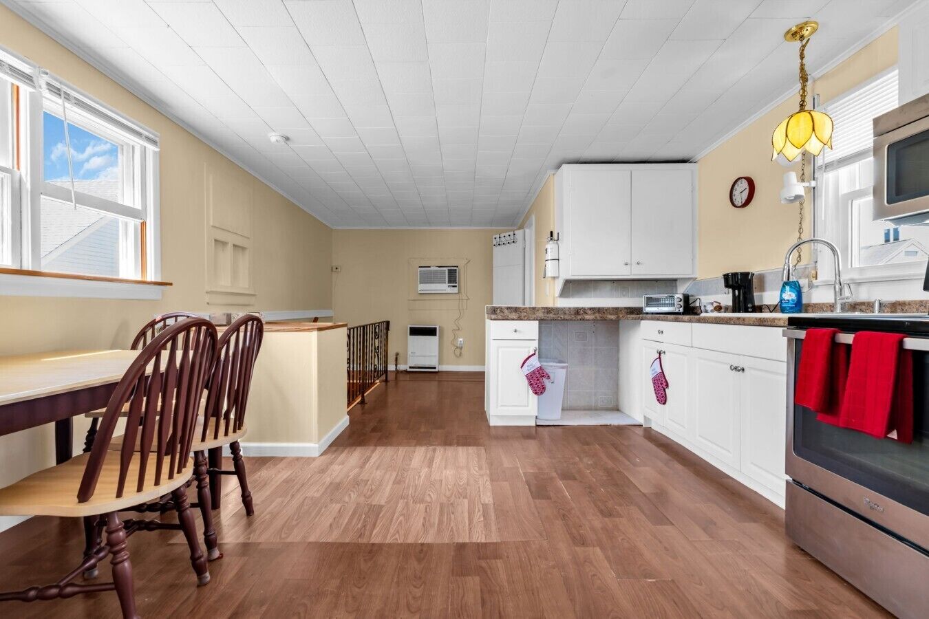 A kitchen with wooden flooring, white cabinets, a dining area with chairs, and a hanging light fixture.