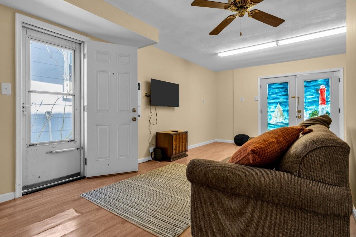 Un salon avec un ventilateur de plafond, un téléviseur, un meuble en bois, un canapé et un tapis.