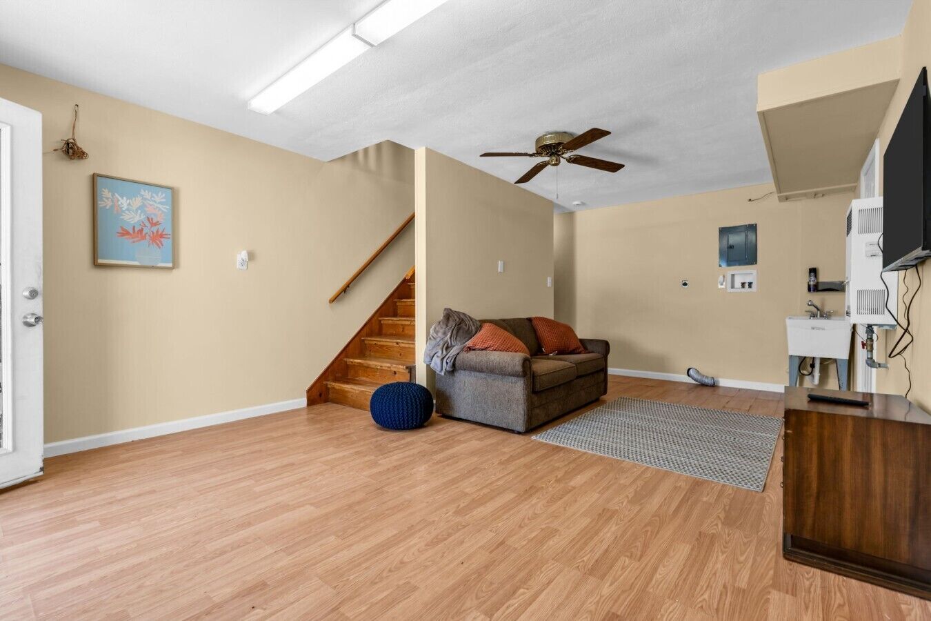 Een ruime woonkamer met een houten vloer, een bank, een plafondventilator en een trap.