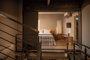 A modern hotel room with a bed, a bedside table, a TV, and a staircase leading to another room.