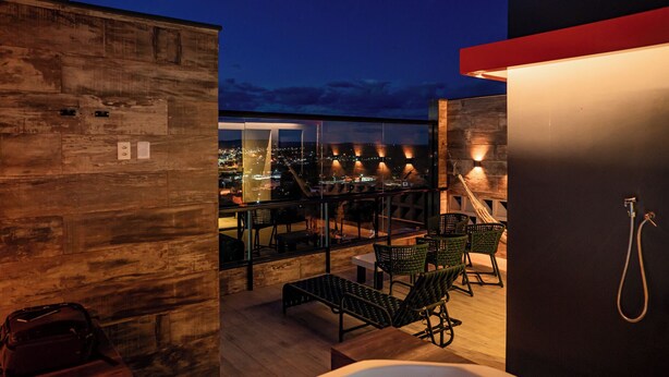 A rooftop terrace with a view of the city at night, featuring a hot tub, outdoor seating, and a hammock. - Exclusive Loft | Rooftop with Panoramic Views (São Raimundo Nonato)
